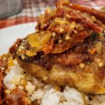 Pan seared chicken thighs over sushi rice with sun dried tomatoes, garlic, onions, and a cream sauce on a porcelain dinner plate.