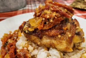 Pan seared chicken thighs over sushi rice with sun dried tomatoes, garlic, onions, and a cream sauce on a porcelain dinner plate.