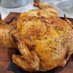 Roast chicken sitting on a wooden cutting board.