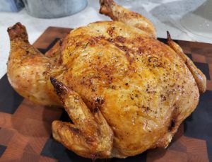 Roast chicken sitting on a wooden cutting board.